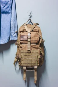 Tan tactical backpack with a U.S. flag patch hanging on a wall hook