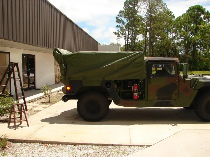 Military Humvee parked outside the shop with a custom olive cargo cover over its bed