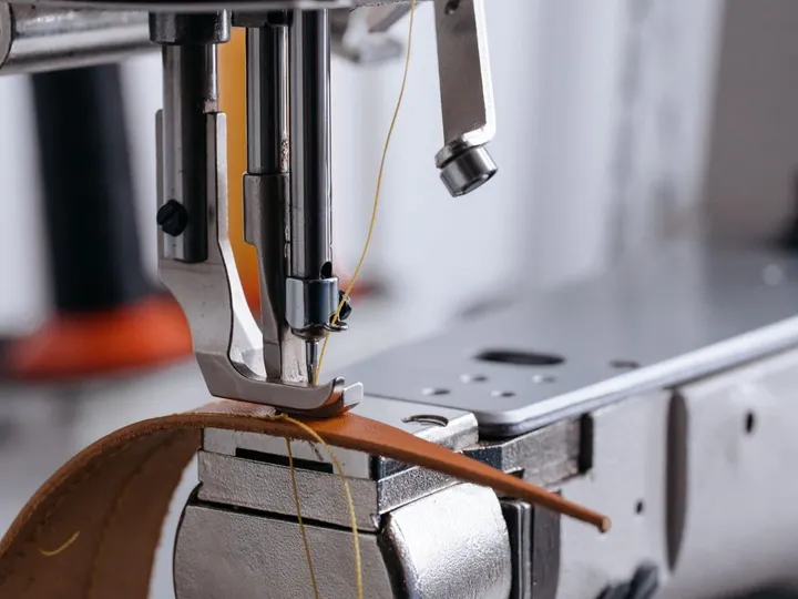 Industrial sewing machine needle stitching a tan leather strap