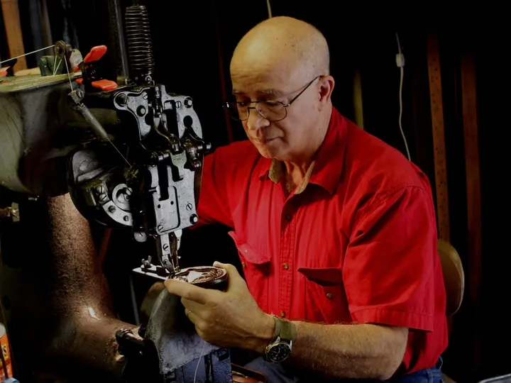 Founder Tim Kennedy in a red shirt guiding leather through a sewing machine at the shop